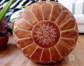 May include: A brown leather pouf with white stitching and a white embroidered star design. The pouf is round and has a tufted top.