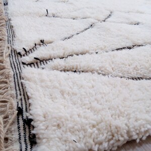 May include: White fluffy rug with a black and white striped border. The rug has a geometric pattern woven into the fabric.