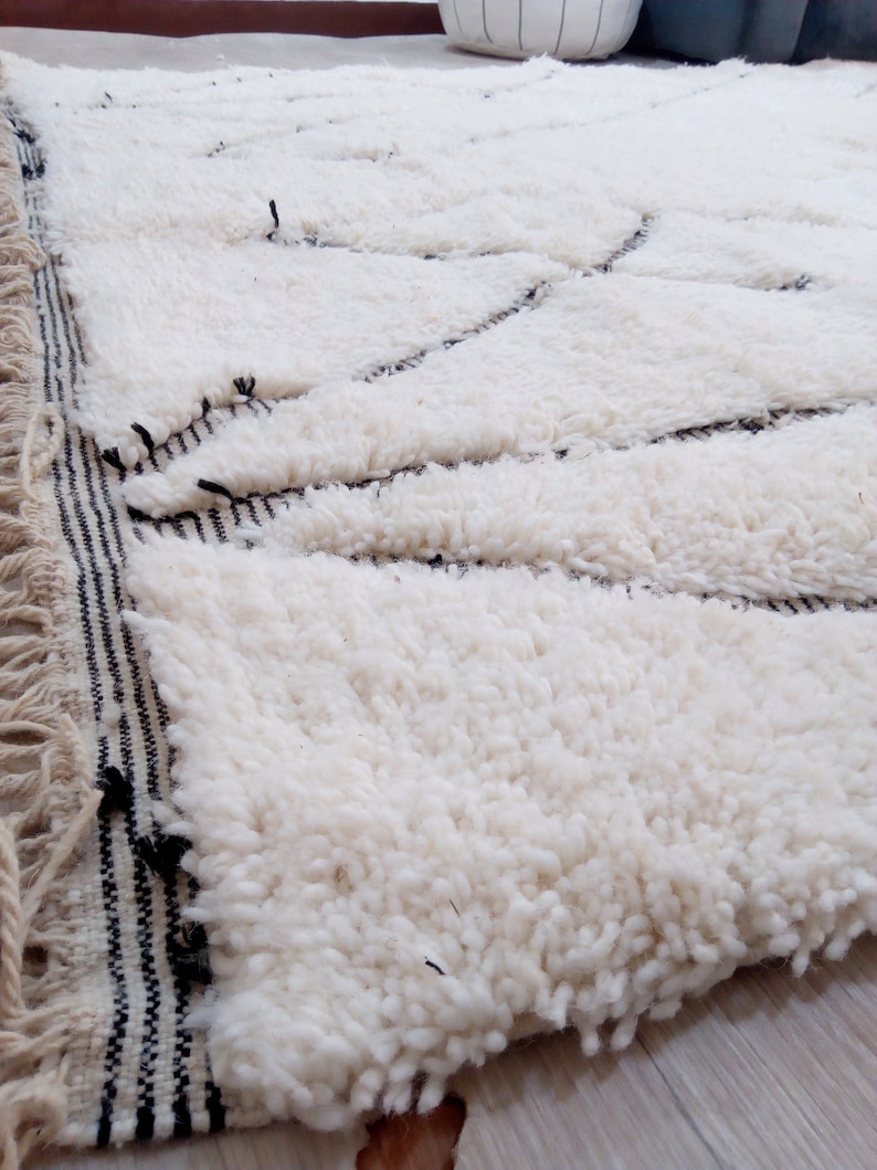 May include: White fluffy rug with a black and white striped border. The rug has a geometric pattern woven into the fabric.