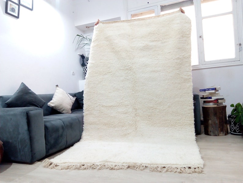 Pode incluir: Um tapete branco de pelo alto com uma borda de franjas. O tapete est&aacute; sendo segurado pelas m&atilde;os de uma pessoa.