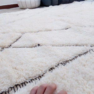 May include: A white shag rug with a geometric pattern in black. The rug is made of soft, fluffy fibers and has a luxurious feel.