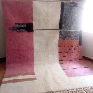 May include: A white, pink, and black geometric patterned rug with a fringe border. The rug has a modern design with a mix of colors and textures.