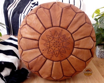 May include: A brown leather pouf with a star-shaped design in the centre. The pouf is made of multiple leather panels stitched together.