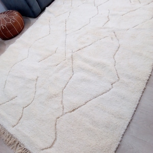 Puede incluir: Una alfombra de pelo blanco con un patr&oacute;n geom&eacute;trico en un tono de blanco m&aacute;s claro. La alfombra tiene un borde de flecos.