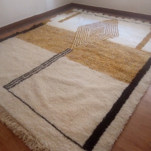 Puede incluir: Una alfombra geom&eacute;trica blanca, crema y marr&oacute;n con ribete negro. La alfombra tiene un borde de flecos.