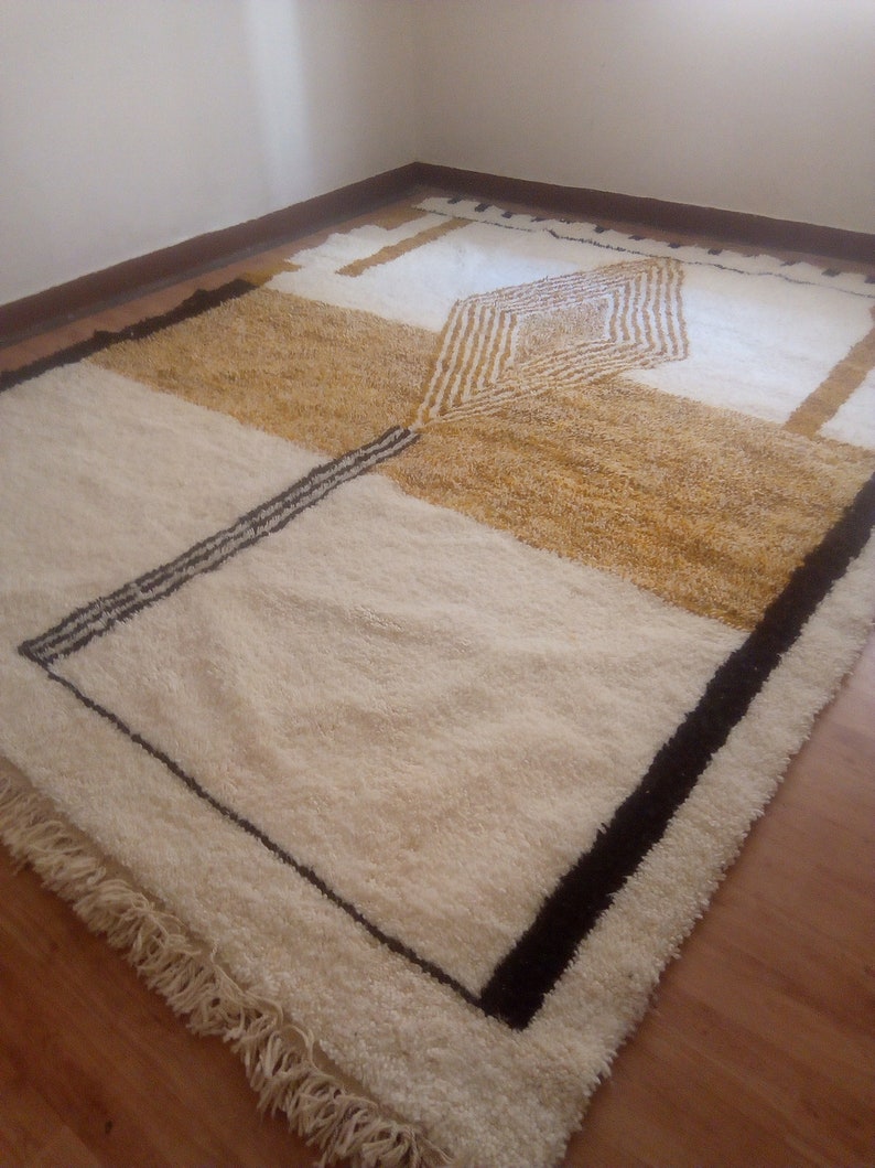 Puede incluir: Una alfombra geom&eacute;trica blanca, crema y marr&oacute;n con ribete negro. La alfombra tiene un borde de flecos.
