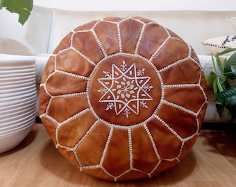 May include: A brown leather pouffe with white stitching and a white embroidered star design.
