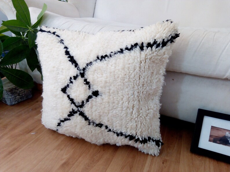May include: White and black geometric patterned throw pillow with a fluffy texture. The pillow is on a wooden floor.