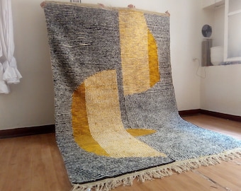 Pode incluir: Um tapete grande tecido à mão com um design geométrico em tons de preto, branco e amarelo. O tapete tem uma borda de franjas e é feito de lã.