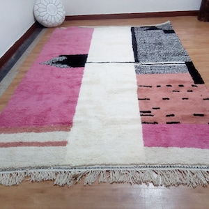 May include: A white, pink, and black geometric patterned rug with a fringe border. The rug has a modern design with abstract shapes and lines.