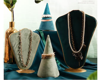 May include: Three velvet jewelry display stands in teal and green with gold accents. The stands are shaped like a cone, a bust, and a heart. Each stand is displaying a necklace and a bracelet.