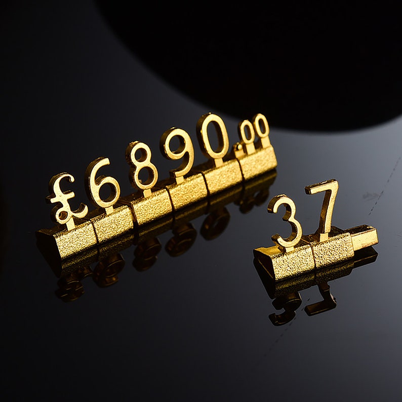 May include: Gold-colored number and symbol display stands. The stands are made of metal and have a textured surface. The numbers are 6, 8, 9, 0, 0, 0, 3, and 7. There is also a pound symbol.