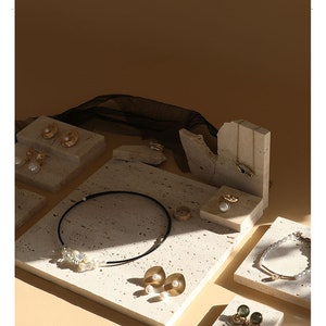May include: A set of six beige stone jewelry display stands with various shapes and sizes. The stands are arranged on a beige background and feature a variety of gold and pearl jewelry.