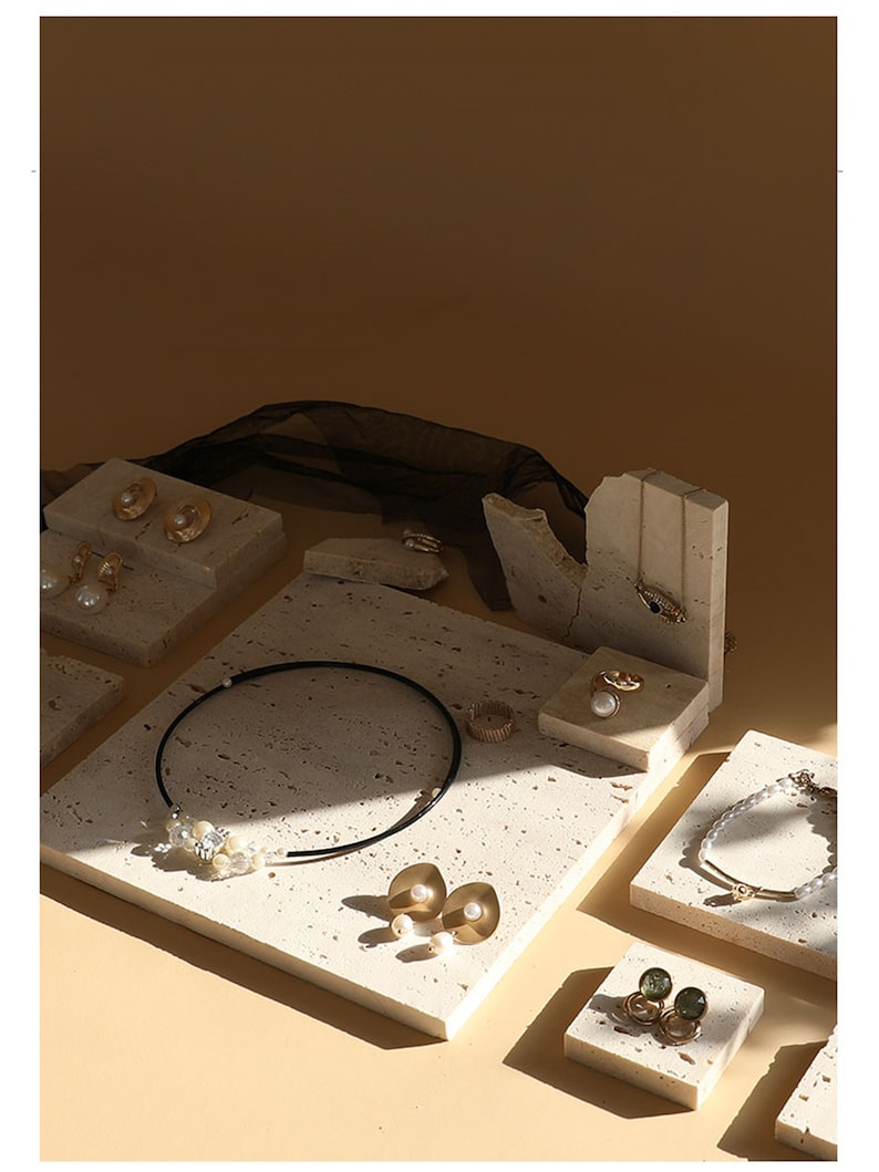 May include: A set of six beige stone jewelry display stands with various shapes and sizes. The stands are arranged on a beige background and feature a variety of gold and pearl jewelry.