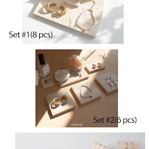 May include: Three sets of small, square, beige, textured display trays with gold jewelry on them. The jewelry includes earrings, necklaces, and rings. The trays are arranged in a grid pattern. The text "Set #1 (8 pcs)", "Set #2 (6 pcs)", and "Set #3 (11 pcs)" is visible below each set of trays.
