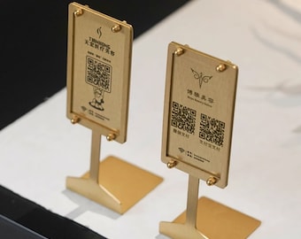 May include: Two gold metal stands with square bases and a vertical post. Each stand has a rectangular sign with a black and white QR code and text in Chinese. The sign on the left says "Tianhong" and the sign on the right says "Happy Beauty Salon".