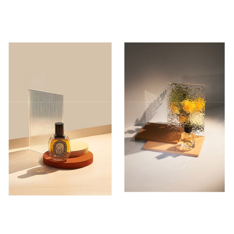 May include: A brown glass bottle of perfume with a black cap sits on a brown and beige circular platform. The bottle is in front of a textured glass panel.