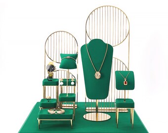May include: A gold metal jewelry display stand with a green velvet base and multiple levels for displaying necklaces, earrings, rings, and watches.