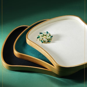 May include: Three nested trays with gold rims. The top tray is white, the middle tray is green, and the bottom tray is black. A small jeweled pin is on the white tray.