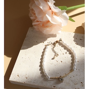 May include: A delicate gold bracelet with a single crystal charm and a row of white faux pearls.