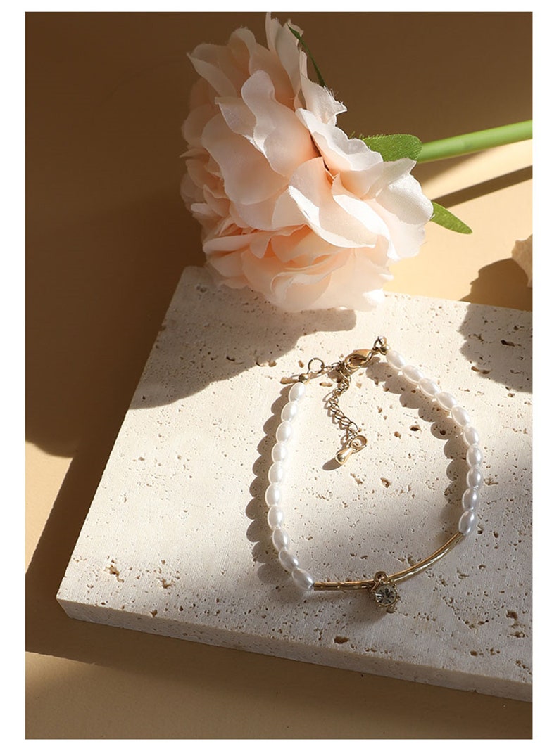 May include: A delicate gold bracelet with a single crystal charm and a row of white faux pearls.