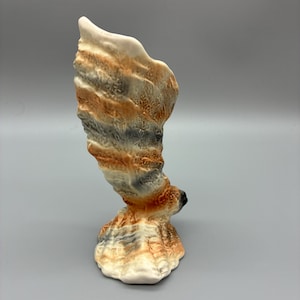 May include: A ceramic sculpture with an abstract, swirling design. It has a base and a tall, upward-reaching form. The colours include white, orange, grey, and black, creating a textured, layered appearance. The sculpture is likely a decorative item.