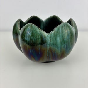 May include: A ceramic bowl with a scalloped, flower-like rim. The exterior features a glossy glaze with a gradient transition from deep forest green at the top to a dark, iridescent brownish-purple hue at the base, creating a smooth finish.