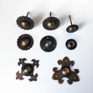 Può includere: Assortimento di otto chiodini decorativi in metallo con vari disegni. I chiodini sono in tonalità di ottone e oro. Alcuni chiodini sono rotondi, mentre altri hanno un design più intricato.