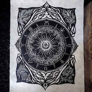 May include: A monochrome art print depicting a central sun motif with an eye, encircled by a wreath and symbols. The design is framed by elaborate floral and geometric patterns, with the words "Wheel of the Year" at the base.