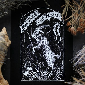 以下が含まれることがあります： 黒と白の刺繍パッチ。頭蓋骨の上に立っているヤギが、「Kein Bock auf Nazis」と書かれたバナーを持っています。