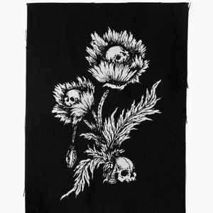 May include: Black and white embroidered patch featuring a bouquet of three stylized flowers with skulls in the center of each bloom. The flowers have a spiky, flame-like appearance.