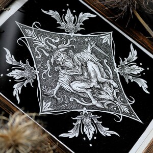 May include: A black and white print of a horned figure with a dagger, surrounded by ornate floral designs. The print is framed in a dark wood frame.