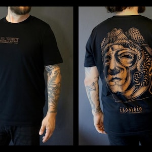 May include: Black t-shirt with a graphic print of a person's face on the back. The text "ikosisbio" is printed below the graphic. The front of the shirt has the text "The Tramway, Siberia, Moscow" printed in small letters.