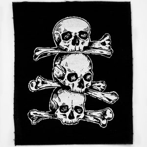 Può includere: Un cerotto di stoffa nero con un disegno bianco di tre teschi impilati con ossa incrociate.