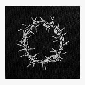 Può includere: Un cerotto di stoffa nero con una corona di spine ricamata in bianco.