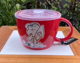 Può includere: Tazza in ceramica rossa con un design di personaggio dei Peanuts. La tazza ha un coperchio in plastica trasparente e un manico. Il personaggio è un cartone animato di un ragazzo che indossa una camicia a righe e tiene una tavola da surf. La tazza ha la scritta "PEANUTS" stampata sul lato.
