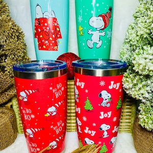 May include: Four stainless steel tumblers with different Christmas-themed designs featuring Snoopy. The tumblers are red, green, and blue.