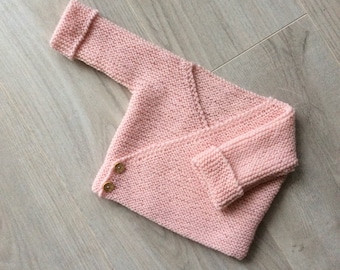May include: A pink knitted baby cardigan with a V-neck and button closure.