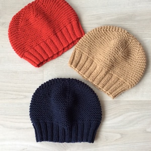 Peut inclure: Trois bonnets en tricot de différentes couleurs : rouge, beige et bleu marine. Les bonnets sont faits avec un point texturé et ont un design simple et classique.