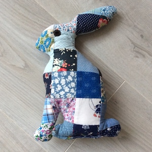 Peut inclure: Un jouet de lapin en patchwork fait de tissu bleu, blanc et rose avec des motifs floraux et géométriques.