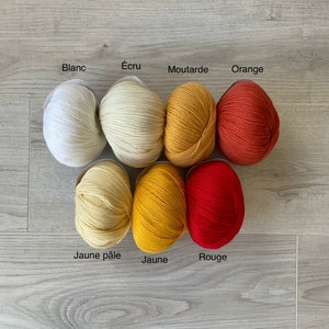 May include: Balls of yarn in various shades of yellow, orange, and red. The yarn is labeled with French words for each color: Blanc, &Eacute;cru, Moutarde, Orange, Jaune p&acirc;le, Jaune, and Rouge.