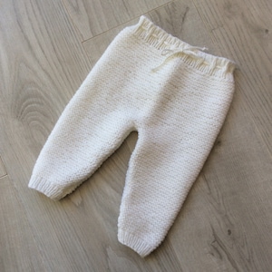 Peut inclure: Pantalon bébé en tricot blanc avec une taille à cordon.