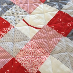 Peut inclure: Une courtepointe rouge, blanche et grise avec un motif en losange. La courtepointe est faite de différents tissus avec divers motifs, notamment des pois, des rayures et des motifs floraux.