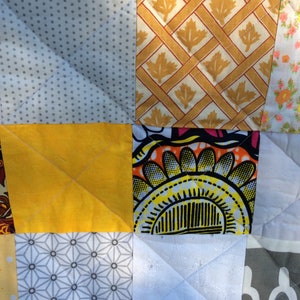 Könnte beinhalten: Eine Patchwork-Decke mit verschiedenen Mustern und Farben, darunter Gelb, Grau, Weiß und Schwarz. Die Decke besteht aus Quadraten aus verschiedenen Stoffen, die jeweils ein einzigartiges Design haben.