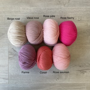 May include: Eight balls of yarn in various shades of pink, beige, and coral. The yarn balls are labeled with their French names: Beige ros&eacute;, Vieux rose, Rose p&acirc;le, Rose flashy, Parme, Corail, Rose saumon.