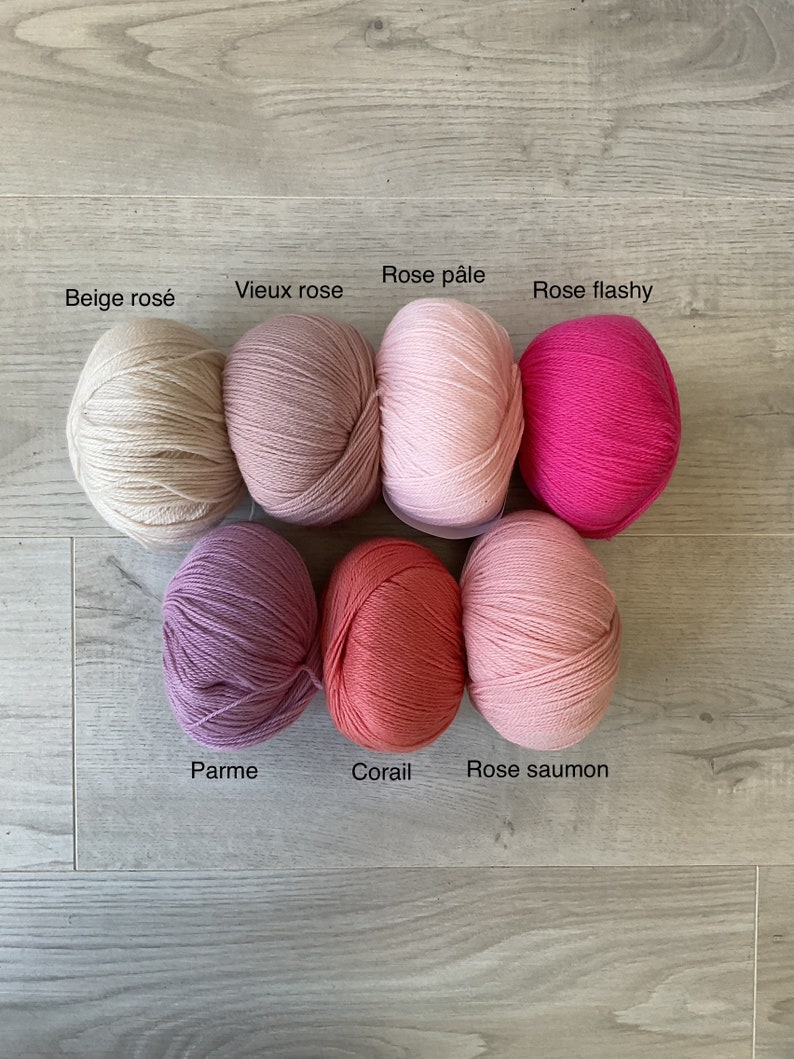 May include: Eight balls of yarn in various shades of pink, beige, and coral. The yarn balls are labeled with their French names: Beige ros&eacute;, Vieux rose, Rose p&acirc;le, Rose flashy, Parme, Corail, Rose saumon.