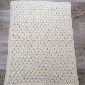 May include: A white crocheted baby blanket with a delicate openwork pattern.