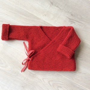 Puede incluir: Un jersey de punto rojo para bebé con estilo envolvente y un lazo rojo.