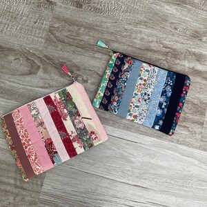 Peut inclure: Deux pochettes rectangulaires en tissu avec fermetures éclair et tirettes à pompon. L'une présente des bandes de tissu roses, rouges et marron. L'autre a des bandes de tissu bleues, vertes et blanches. Les deux sont sur une surface en bois.