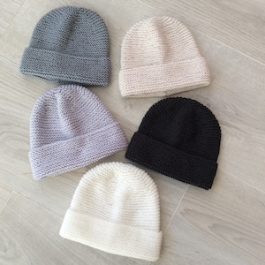 Peut inclure: Cinq bonnets en tricot de différentes couleurs : gris, beige, gris clair, noir et blanc. Les bonnets sont tous du même style, avec un bord simple et plié.